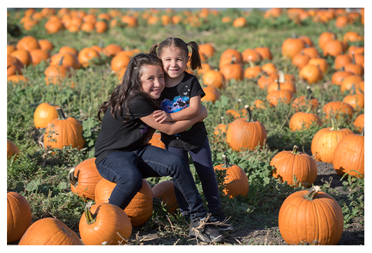 Sisters hugging each other at the pumpkin patch